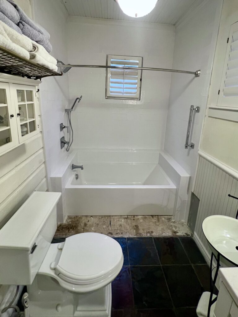 Custom bathroom remodeling in Utah — remodeled bathtub area with new white wall tile, upgraded showerhead, safety grab bars, and a custom tiled ledge for storage.