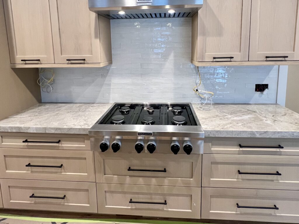 Newly installed glossy white subway-tile backsplash behind a stainless-steel cooktop and light wood cabinets, completed as part of custom remodeling work in Utah.