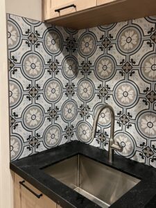 Decorative patterned tile backsplash installed above a stainless steel sink with light wood cabinets — custom home remodeling in Utah.