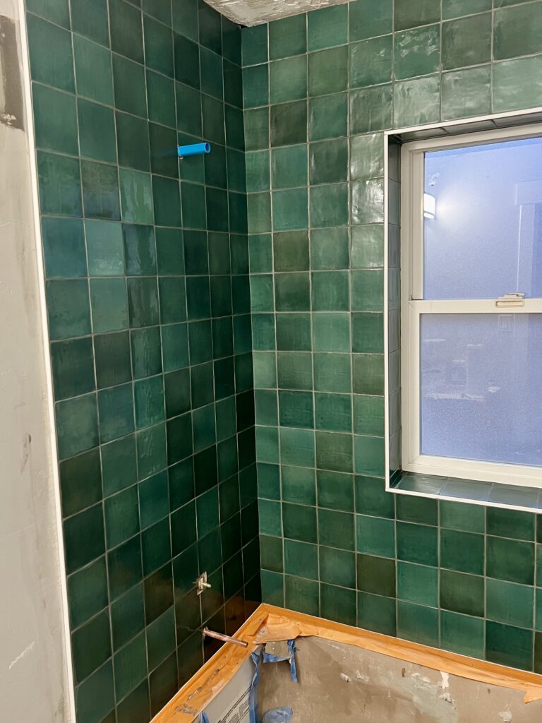 Handcrafted emerald-green tile installation around a bathtub area with full-height coverage and window trim detailing, completed as part of custom bathroom remodeling in Utah.