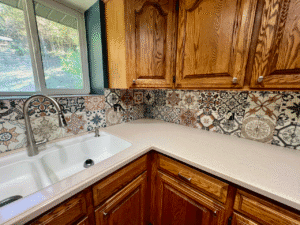 Mediterranean-style patterned tile backsplash installation behind a kitchen sink and countertops, featuring mixed decorative tiles and precise finishing as part of custom remodeling in Utah.