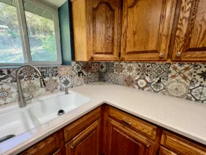 Mediterranean-style patterned tile backsplash installation behind a kitchen sink and countertops, featuring mixed decorative tiles and precise finishing as part of custom remodeling in Utah.
