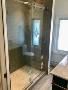 Luxury gray tile walk-in shower with sliding glass door, gold fixtures, and corner bench — Custom bathroom remodeling in Utah.
