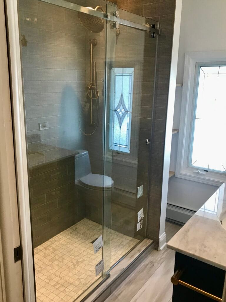 Luxury gray tile walk-in shower with sliding glass door, gold fixtures, and corner bench.