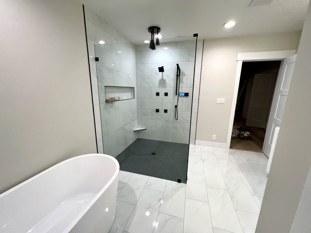Modern walk-in shower with marble-look wall tiles, black fixtures, a built-in niche and a free-standing bathtub — Custom Bathroom Remodeling in Utah.